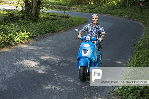 Kaukasischer Mann fährt blauen Motorroller