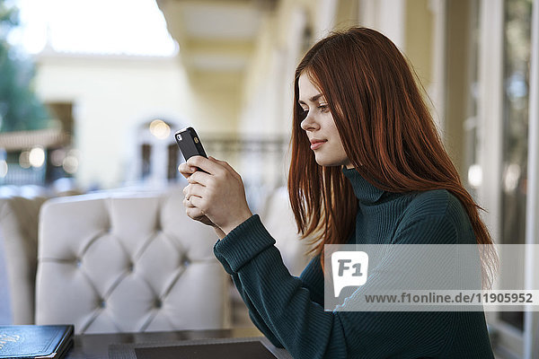 Kaukasische Frau  die in einem Restaurant eine SMS auf ihrem Handy schreibt