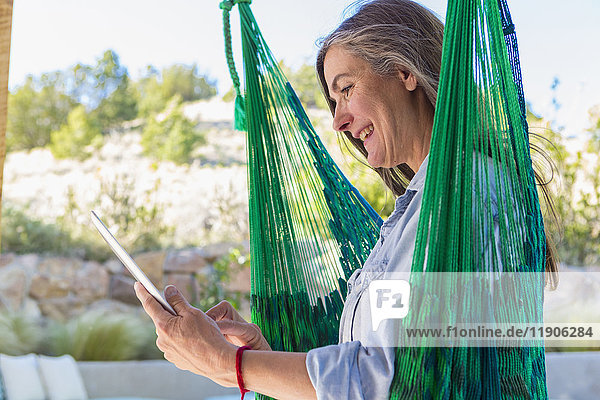 Ältere kaukasische Frau liest digitales Tablet in grüner Hängematte