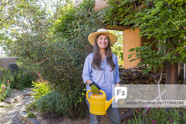 Ältere kaukasische Frau hält Wasserkanister im Garten