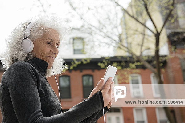 Ältere Frau hört mit Kopfhörern in der Stadt Handy