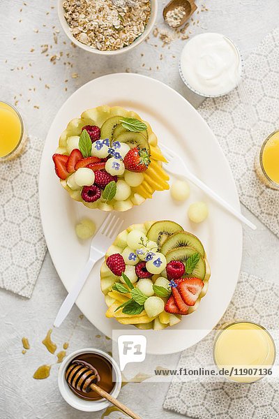 Ein gesundes Frühstück: Obstsalat  serviert in Melonenhälften  Joghurt  Müsli  Orangensaft und Honig