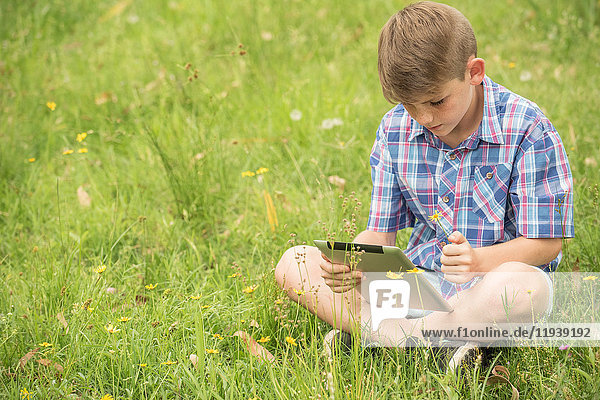 Junge auf Gras sitzend,  mit digitalem Tablett