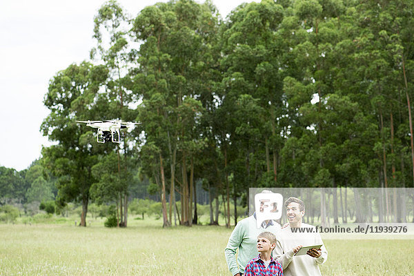 Mann fliegt ferngesteuerte Drohne im offenen Feld  während ältere Männer und Jungen zusehen.