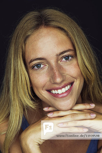 Young woman smiling with hands clasped under chin  portrait