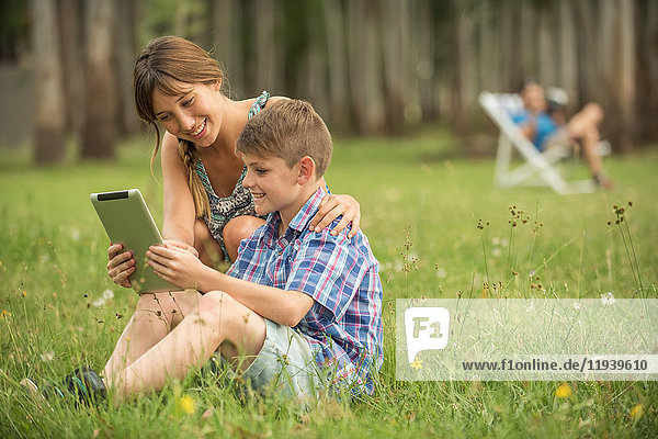 Mutter und Sohn benutzen gemeinsam ein digitales Tablett im Freien.