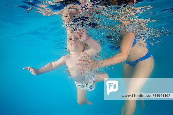 Mom learns little boy to dive underwater in the pool.