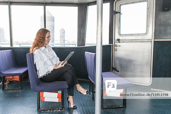Stilvolle junge Geschäftsfrau betrachtet digitales Tablet auf Passagierfähre