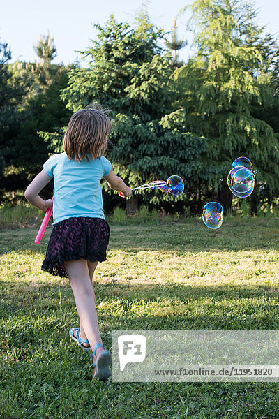 Junges Mädchen spielt mit dem Blasenzauberstab im Garten,  Rückansicht