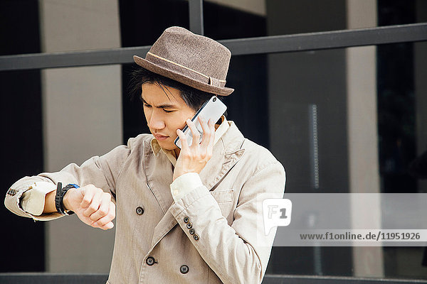 Young man outdoors  using smartphone  looking at wristwatch