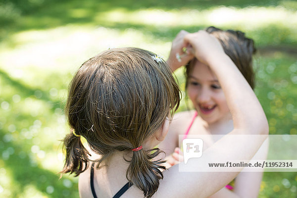Junges Mädchen steckt Gänseblümchen in die Haare der Schwester  im Freien
