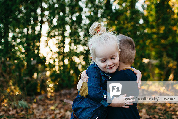 Süßes weibliches Kleinkind umarmt Zwillingsbruder im Herbstgarten