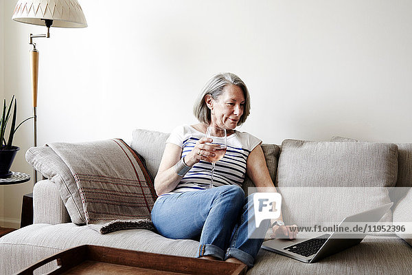 Senior woman with grey bob sitting on sofa looking at laptop
