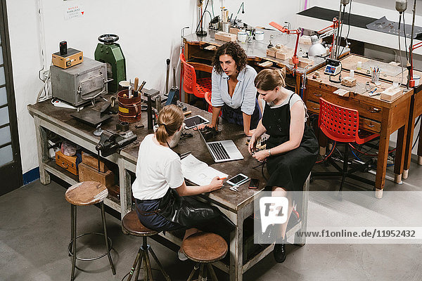 High angle view of three female jewellers having discussion at workbench meeting