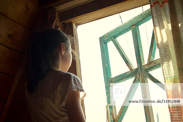Teenager-Mädchen schaut aus dem sonnenbeschienenen Schlafzimmerfenster