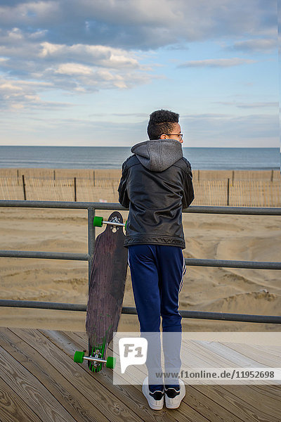 Junge lehnt an der Reling  schaut auf Aussicht  Skateboard neben ihm  Asbury  New Jersey  USA