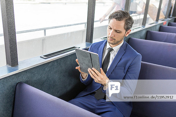 Young businessman on passenger ferry looking at digital tablet