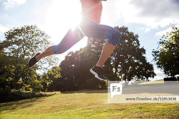 Blick von der Hüfte abwärts auf eine junge Frau  die im Park trainiert und im Sonnenlicht durch die Luft springt