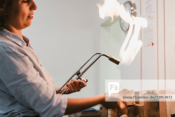 Female jeweller using flaming blow torch at workbench