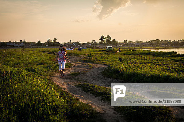 Lone teenage girl running along rural dirt track at sunset