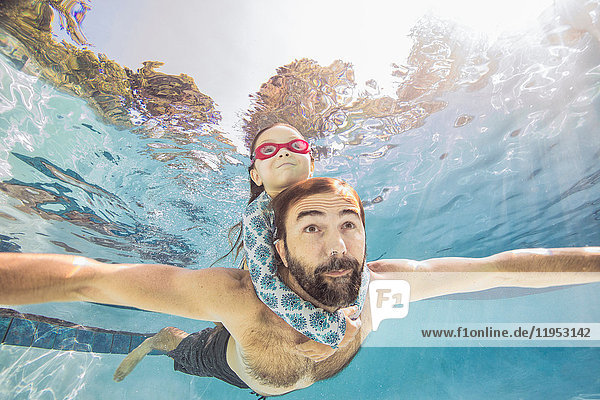 Unterwasseransicht eines reifen Mannes, der mit der Tochter auf dem Huckepack schwimmt