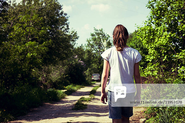 Rückansicht eines Teenager-Mädchens  das auf einem ländlichen Feldweg spazieren geht