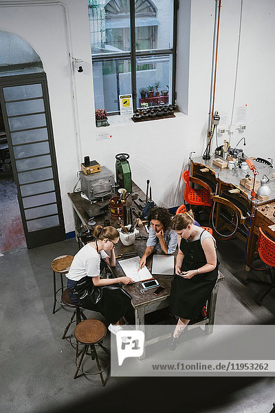 Hochwinkelansicht von drei Juwelierinnen  die bei einem Arbeitstreffen auf den Skizzenblock schauen