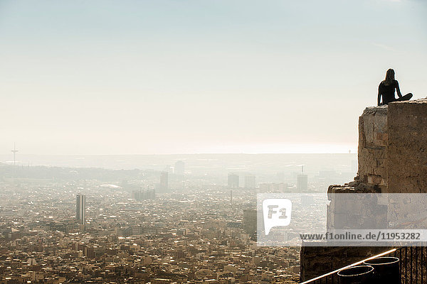 Von hinten beleuchtete weibliche Touristin  die von der Spitze einer Mauer auf das Stadtbild von Barcelona blickt  Spanien