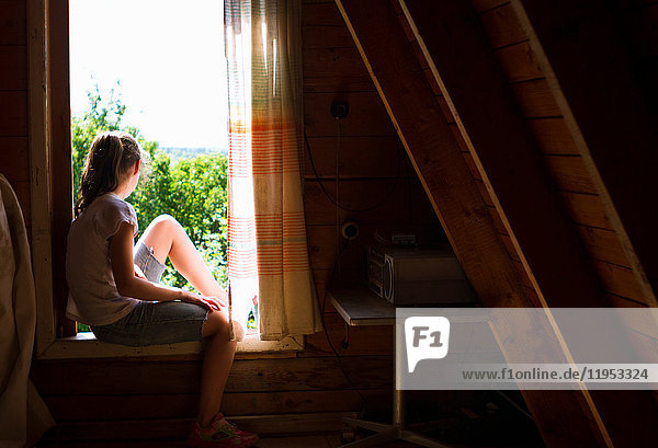 Teenager-Mädchen sitzt auf der Fensterbank im Schlafzimmer und schaut auf das Sonnenlicht