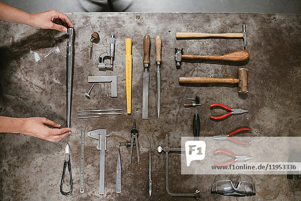 Overhead view of female jeweller's hands laying out hand tools at workbench