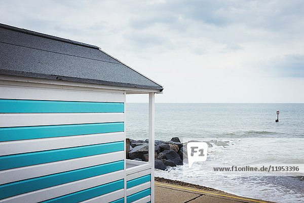 Eine blau-weiß gestreifte Strandhütte an einem Strand an der Küste.