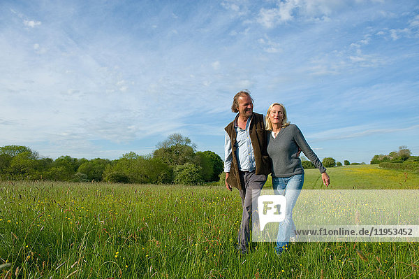 Man and woman walking arm in arm across a meadow.