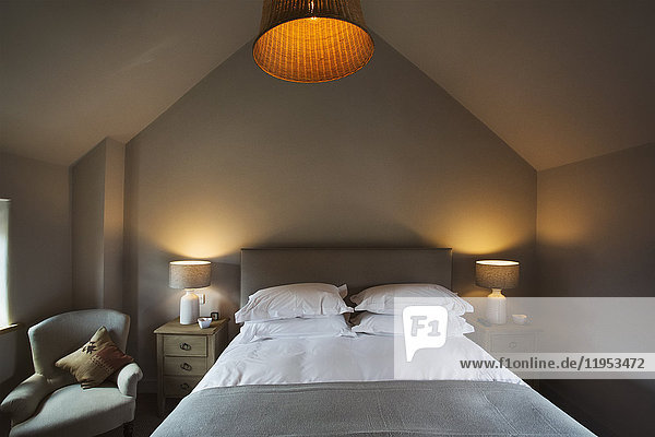 Ein gemütliches  in neutralen Farben dekoriertes Schlafzimmer mit einem Doppelbett und eingeschalteter Nachttischbeleuchtung. Gastfreundschaft.