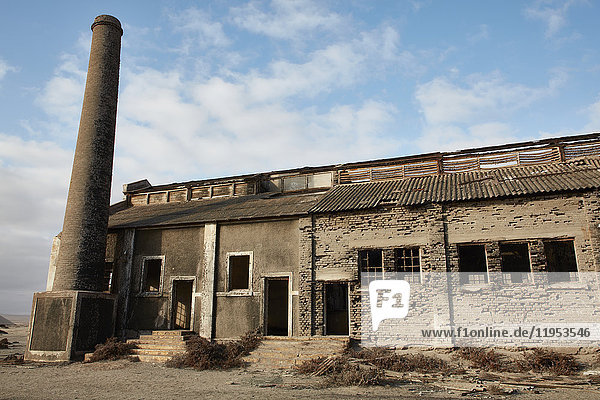 Außenansicht eines verlassenen Gebäudes und eines Industrieschornsteins.