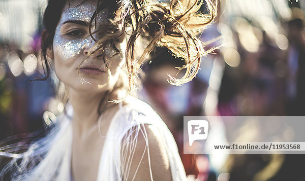Junge Frau mit langen braunen Haaren bei einem Sommer-Musikfestival mit geschminktem Gesicht  in die Kamera lächelnd.