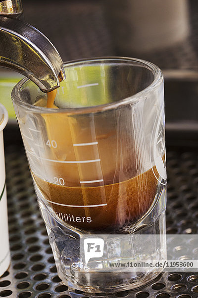 Nahaufnahme von frisch gebrühtem Espresso-Kaffee  der aus einer Kaffeemaschine in ein Glas gegossen wird.