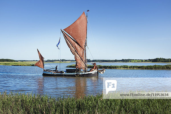 Traditionelles Segelboot mit roten Segeln und einem Gaffelrigg  ein Segelschlag auf dem Wasser auf einem Schilfgürtel oder einer Flussmündung.
