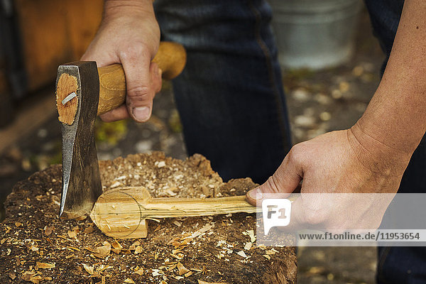 Close up of person holding a hand axe  cutting and shaping a small piece of wood on a splitting block covered in wood shavings.