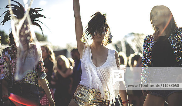 Young woman at a summer music festival wearing golden sequinned hot pants  dancing among the crowd.