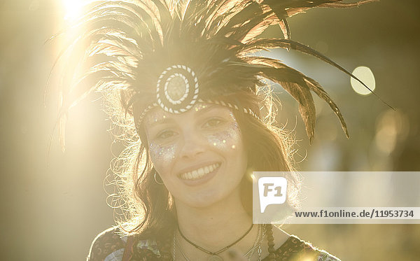 Junge Frau bei einem Sommer-Musikfestival mit Federkopfschmuck und bemaltem Gesicht  lächelt in die Kamera.