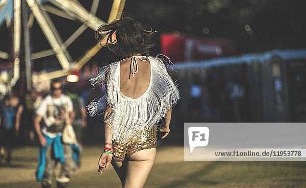Rückansicht einer jungen Frau auf einem Sommer-Musikfestival in goldenen,  mit Pailletten bestickten Hotpants.