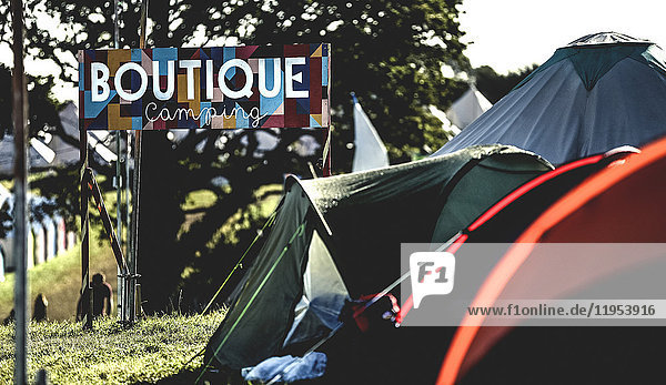 Zelte auf Gras auf einem Campingplatz bei einem Musikfestival im Freien im Sommer. Schild mit der Aufschrift Boutique Camping. Glitzern.