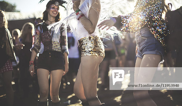 Junge Frau bei einem Sommer-Musikfestival  die in goldenen  mit Pailletten bestickten Hotpants unter der Menge tanzt.