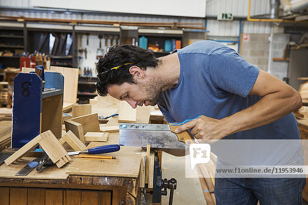 Mann in der Werkstatt eines Bootsbauers  der ein kleines Stück Holz mit der Handsäge sägt.