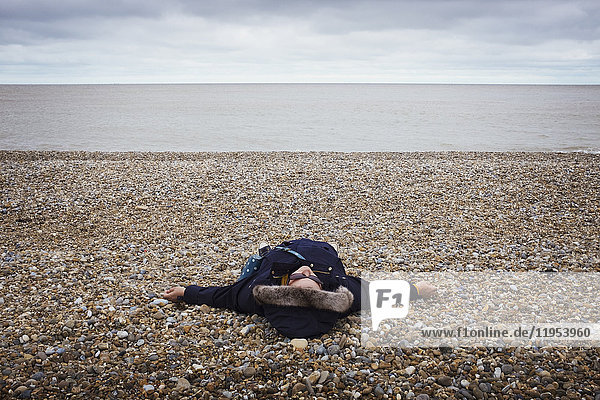 Woman lying on her back on a pebble beach by the ocean.
