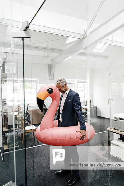 Happy businessman in office with inflatable flamingo