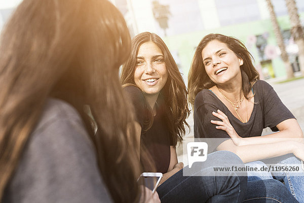 Three happy young women sitting outdoors