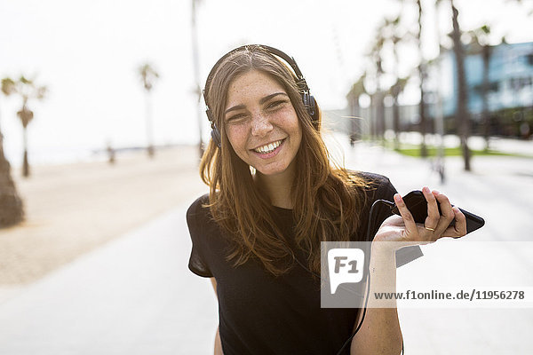 Porträt einer glücklichen jungen Frau an der Strandpromenade beim Musikhören