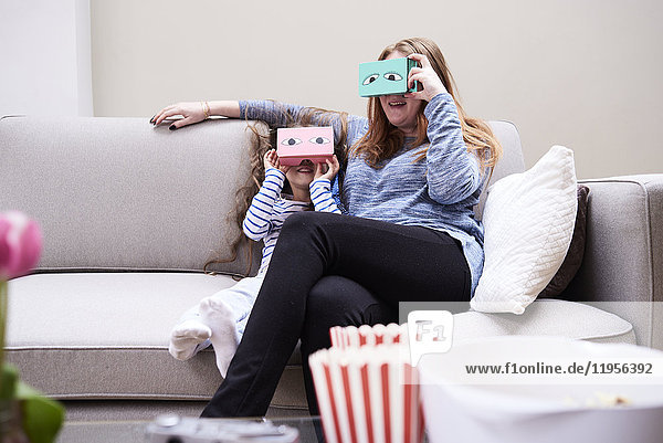 Mutter und Tochter sitzen auf der Couch und haben Spaß mit der Virtual Reality Brille.