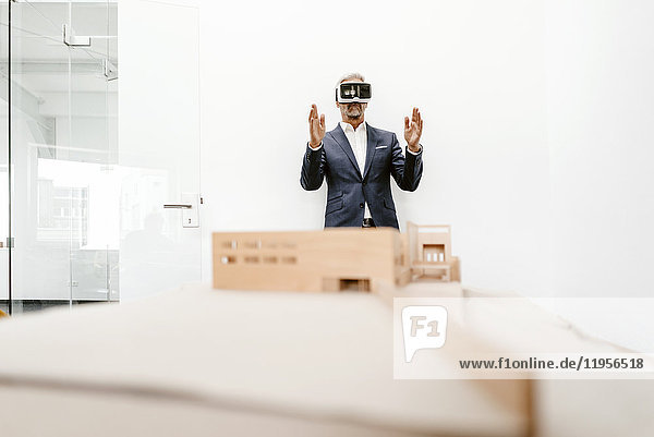 Mature businessman with architectural model in office wearing VR glasses